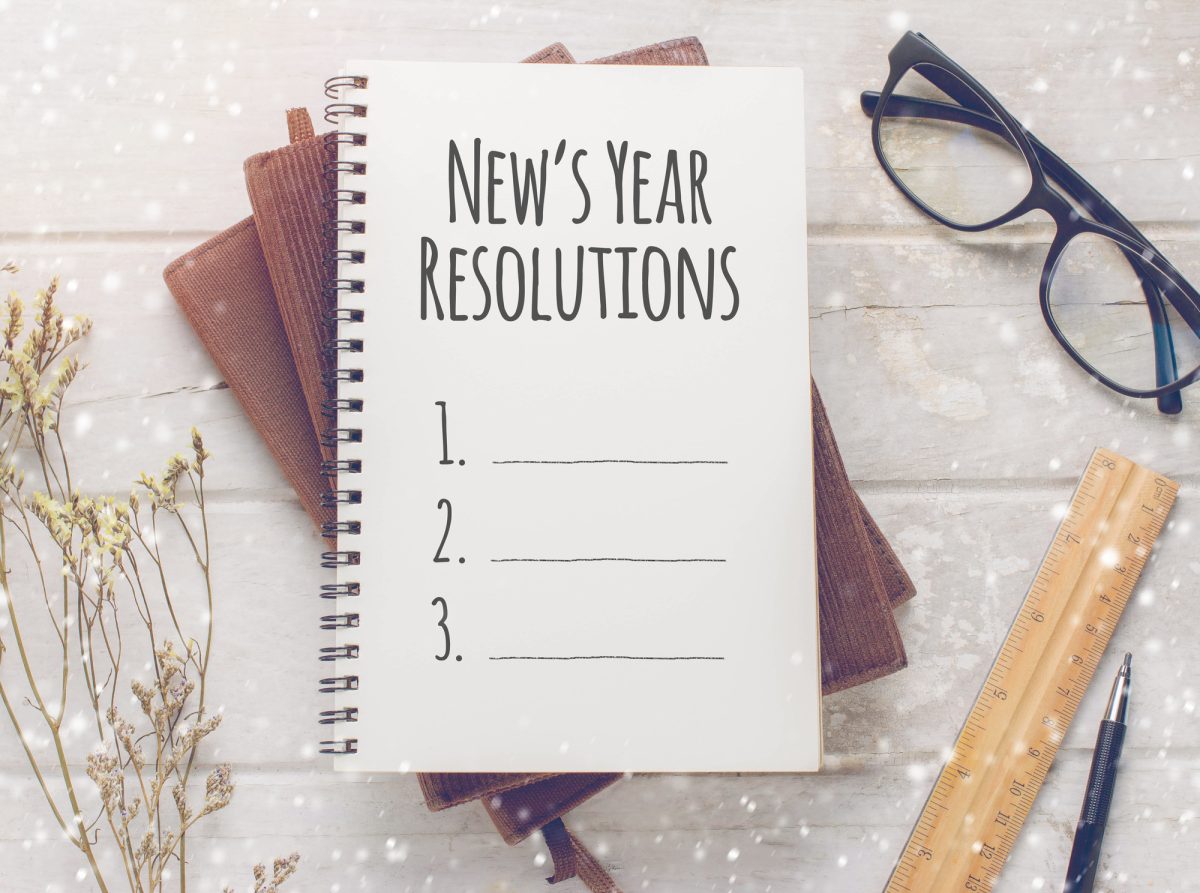 Notebook with News Year Resolutions massage, glasses and working ornament on white wooden table background.